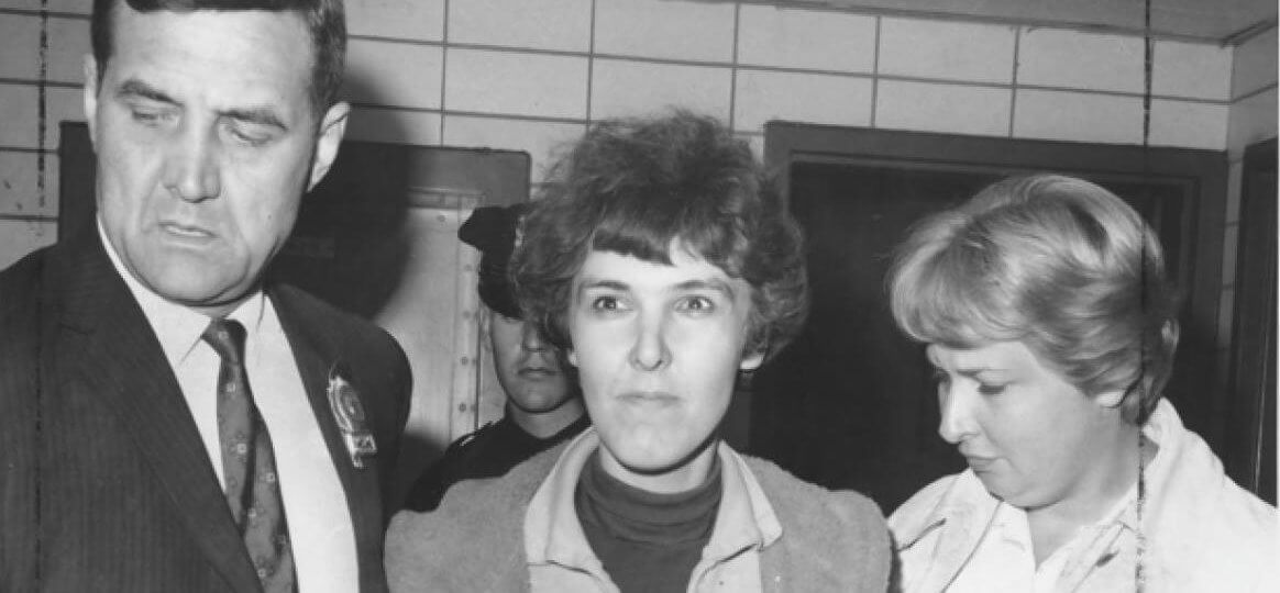 A photo of Valerie Solanas after she had been arrested. A police officer is in the background.