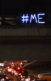 A highway at night with lights on a bridge that Say "#Me Too"