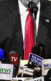 A collage of a photo of Donald Trump from his chin to his midsection with microphones, most of news say "News Channel" on it in front of him.