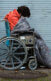 A photo of an unhoused person in a wheelchair and a sleeping bag outside.