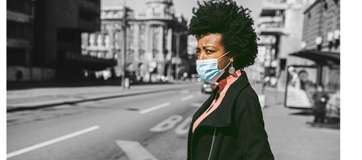 A Black woman wearing a mask on the street of a city