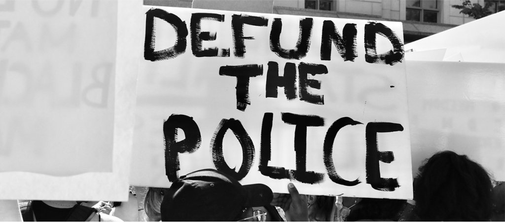 A photo from a protest of a sign that says "Defund the Police."